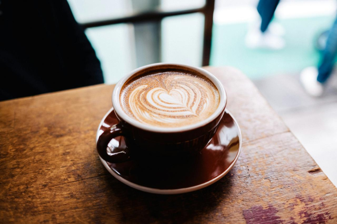 Šolja latte kafe sa srcem od mlečne pene na drvenom stolu Šolja latte kafe sa srcem od mlečne pene na drvenom stolu